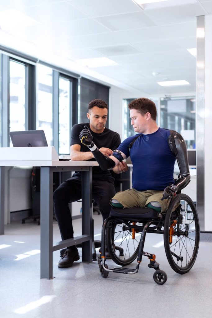 engineer-fitting-prosthetic-arm-3912992 Engineer adjusts prosthetic arm for seated man in wheelchair, focusing on modern technology in healthcare.